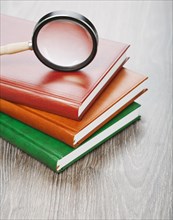 Notebooks and magnifying glass on a wooden background