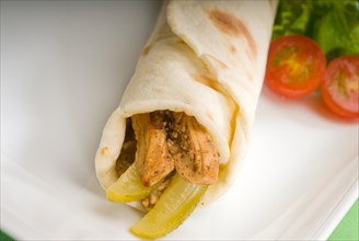 Pita bread chicken roll with pickles cucumbers on a plate with pachino tomatoes and lettuce