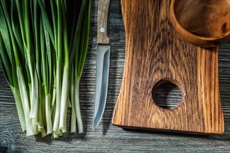 Green spring onion stems kitchen knife wooden chopping board piala on vintage wood background