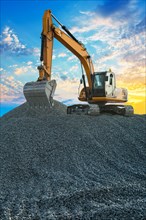 Excavator on large pile of gravel on a background of sunsetly sky