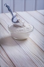 Transparent bowl with flour and shovel on old painted wooden boards