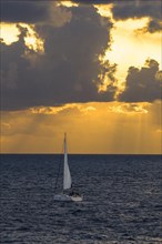 A sailboat on the ocean under a sunset sky with clouds