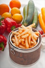 Fresh french fries on a wood bucket with white dip sauce and fresh vegetables on background