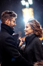 Young beautiful couple in love dancing in the city under snowfall on valentine's day