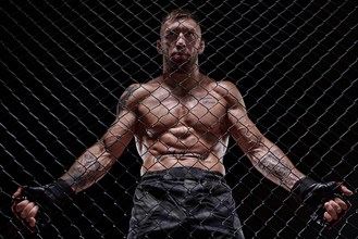 Portrait of a powerful fighter behind the steel bars of the octagon. The concept of sports