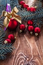 Large composition of Christmas toys red baubles gold coloured bow and branches of fir tree on old wooden board with small copyspace
