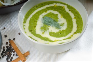 Fresh spinach soup on a white bowl with sage and cream on top