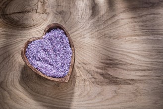 Heart-shaped bowl with lavender sea salt on wood board copy space spa treatment concept