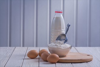 Horizontal view eggs flour in bowl scoop bottle milk on white lacquered old wooden board food and drink concept