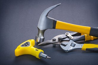 Yellow screwdriver adjustable spanner steel cutter claw hammer on black background