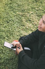 Cheerful teenager of Latino descent smiles as he looks at his smartphone screen. The boy's relaxed posture and cheerful expression convey a sense of contentment. Background blurred to focus attention ...