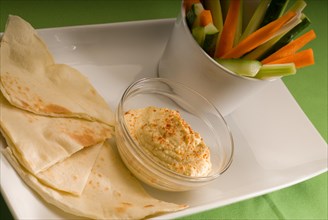 Middle eastern hummus dip on a glass bowl with homemade pita bread and raw vegetable