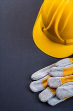 Pair of protective work gloves and yellow helmet on a black background