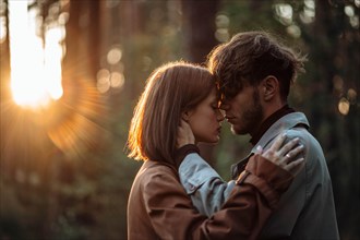 Beautiful fashionable couple in love hugs in the forest at sunset in autumn