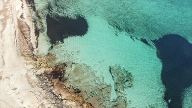 Aerial shot of a rocky coastline with clear turquoise ocean waters