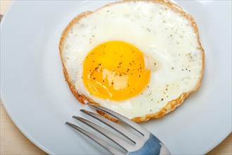 Fried egg sunny side up on a plate with fork over wood table