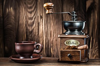 Brown clay coffee cup and vintage wooden mill on old wood background