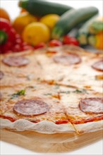 Italian original thin crust pepperoni pizza with fresh vegetables on background