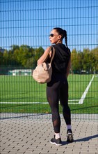 Pretty young fitness girl getting ready for a workout at the stadium. Attractive slim brunette in a tracksuit with a sports bag goes to the locker room. Active lifestyle