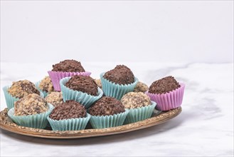 A golden plate with dark rum balls in pastel-coloured paper cups