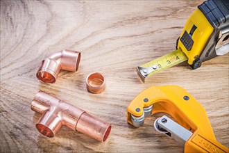 Composition of brass pipe cutter fittings measuring tape on wooden board plumbing concept