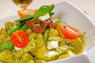 Fresh lumaconi pasta and pesto sauce with vegetables and sundried tomatoes