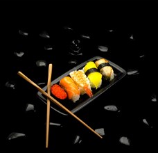 Assorted sushi plate on black pebbles over black background