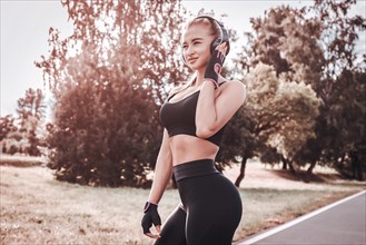 Sports girl in headphones posing in the park. The concept of a healthy lifestyle. Sports Equipment. Fitness style advertisement. Mixed media