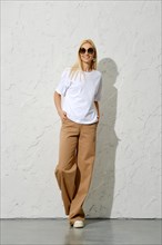 Positive adult woman in brown loose trousers and white shirt posing in the studio