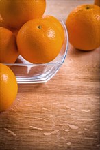 Orange fruit in a square glass bowl on a wooden table