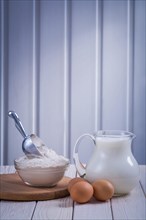 Jug with milk bowl Flour Egg on white lacquered wooden board Food and drink Still life