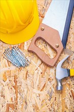 Hard hat nails hand saw claw hammer to plywood panel