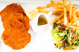 Classic breaded Milanese veal cutlets with french fries and vegetables on background