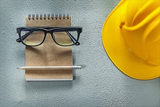 Hard hat glasses notebook pencil on concrete background