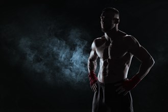 Kickboxer in red bandages poses against a background of smoke. The concept of mixed martial arts. MMA