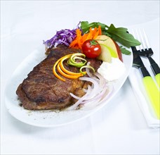Fresh juicy beef ribeye steak grilled with lemon and orange peel on top and vegetables beside with sour cream