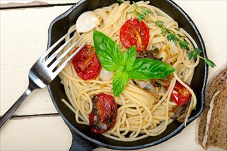 Italian spaghetti pasta with baked tomatoes basil and thyme sauce on a cast iron skillet