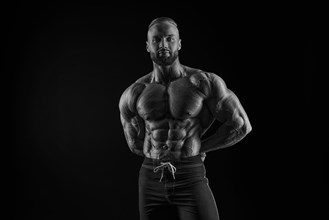 Silhouette of a strong bodybuilder. Confident young fitness athlete with a powerful body and perfect abs. Black and white photography. Dramatic light. Mixed media