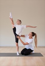 Beautiful female teacher helps a little girl stretch in a gymnastics class. The concept of education