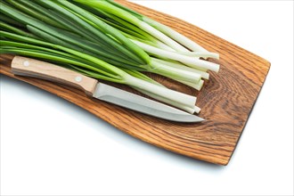Green spring onion scallion stems with kitchen knife on wooden cutting board isolated white