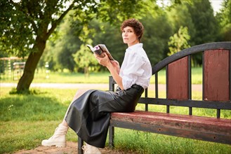 Retro image of a stylish beautiful woman sitting in a park on a bench with a book in her hands. The concept of style and fashion