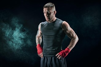 Kickboxer in red bandages stands against a background of smoke. The concept of mixed martial arts. MMA