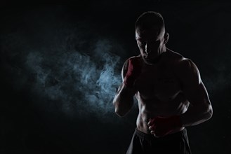 Kickboxer in red bandages poses against a background of smoke. The concept of mixed martial arts. MMA
