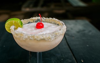 Close up of delicious frozen coconut cocktail with cherry. Frozen coconut margarita with lemon slice served on wooden table