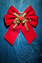 Beautiful red Christmas bow with gold ribbon and bells on an old blue lacquered wooden board
