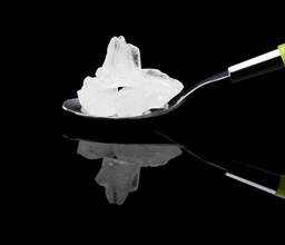 Crystal sugar on a spoon over black reflective surface background