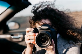 Curly girl in a convertible holds a camera in her hands