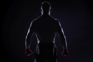 Kickboxer in red bandages posing on a blue background. Back view. The concept of mixed martial arts. MMA