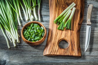 Fresh green spring scallions wooden cutting board kitchen knife vintage wood background