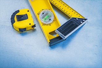 Yellow tape measure construction level and square ruler on metallic background maintenance concept